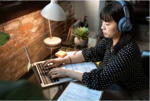 Mulher oriental com fome de ouvido trabalhando no notebook sobre a mesa